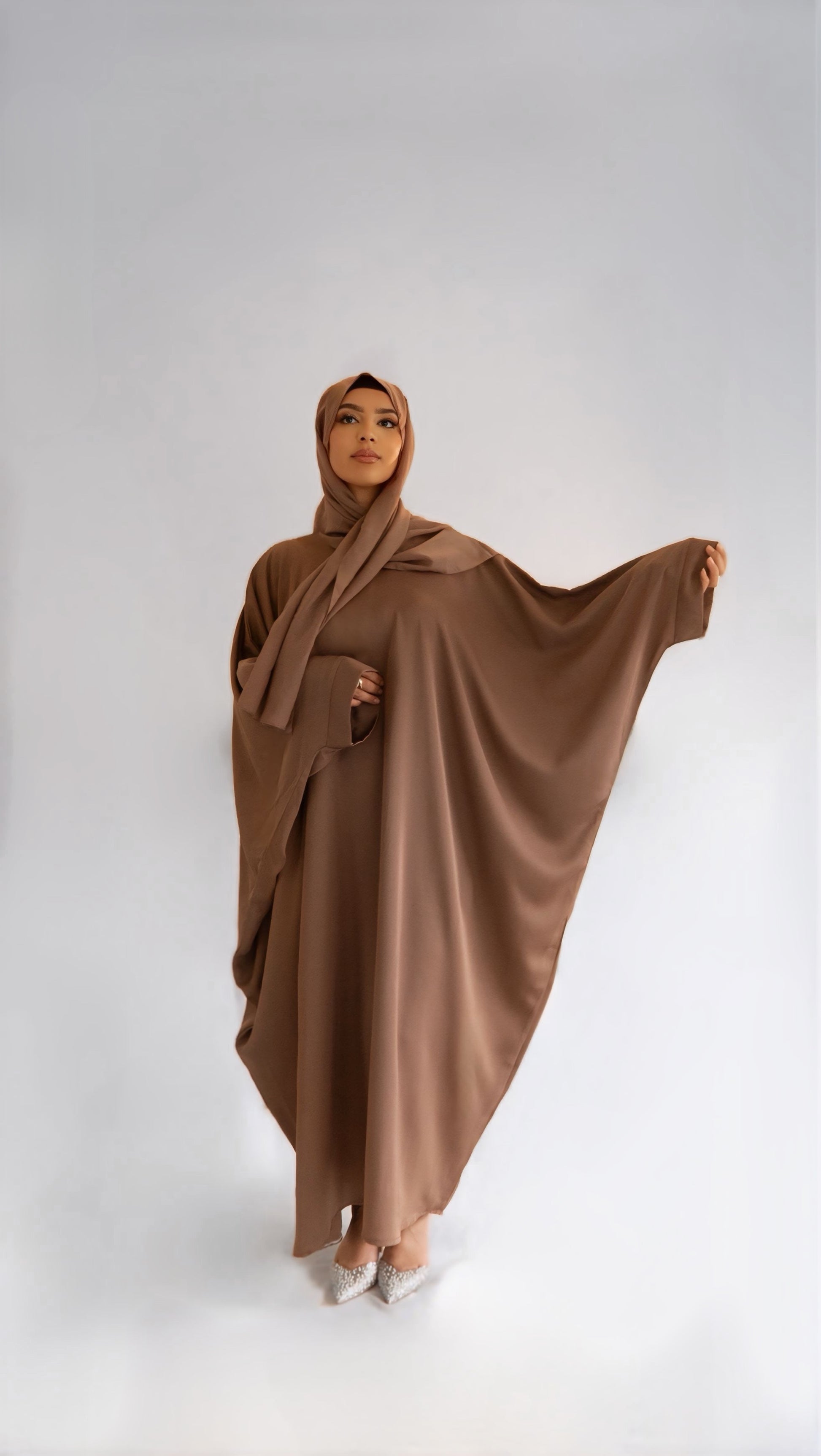 Femme portant la abaya Elegance Batwing, de face, avec le bras gauche levé à hauteur d'épaule